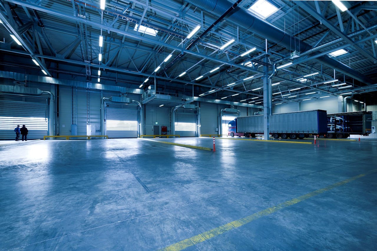 Home Wide view of an empty modern warehouse with industrial lighting and trucks.